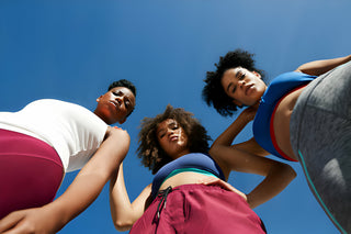 Directly below portrait of confident female friends in sportswear standing against blue sky on sunny day